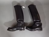 une paire de bottes d'équitation en cuir noir posée sur une table blanche