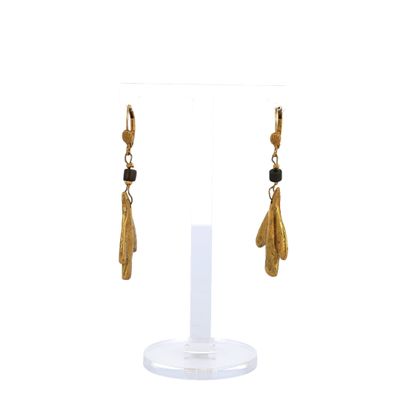 a pair of gold earrings with black beads on a white stand