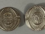 two silver buttons with designs on them sitting on a table