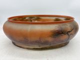 un saladier orange et marron posé sur une table blanche