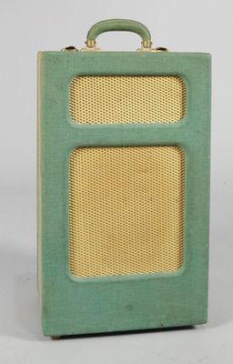 an old green suitcase with a wicker handle sitting on a white surface