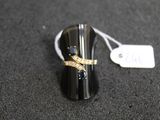 bague noire et dorée sertie de diamants, posée sur une surface noire à côté d'une étiquette de prix