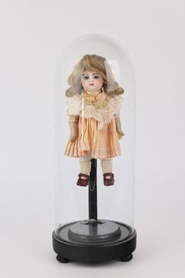 une petite poupée dans une cloche en verre posée sur un socle noir