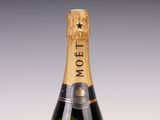 une bouteille de champagne Moët posée sur une surface blanche, avec un fond gris