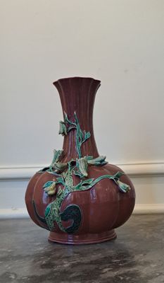 un vase rouge orné de feuilles vertes, posé par terre