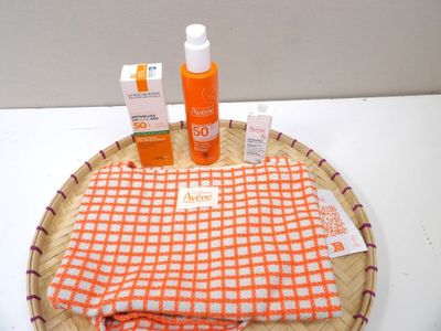 an orange and white towel, a bottle of sunscreen, and a bottle of sunscreen on a wicker tray