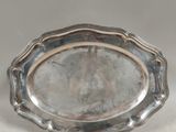 une assiette ancienne en argent sur fond blanc, ornée d'une petite fleur