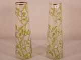 two tall vases with plants in them on a table