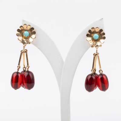a pair of red and gold earrings on a white stand
