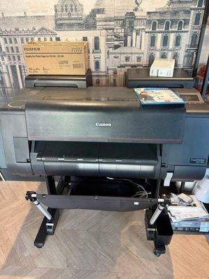 L'imprimante Canon est posée par terre devant un mur, avec en arrière-plan la photo d'un bâtiment.