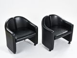 pair of black leather lounge chairs on casteors against a white background