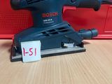une ponceuse orbitale Bosch posée sur une table, à côté d'une boîte rouge