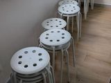 Plusieurs tabourets blancs sont alignés contre un mur dans une pièce