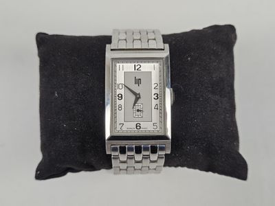 a silver watch on a black pillow on a white surface