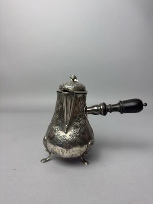 une théière ancienne en argent avec une poignée noire sur une surface blanche