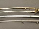 three swords are displayed on a gray surface with a gold handle
