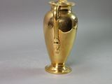 a gold urn with a handle on a white surface