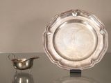 une assiette en argent posée sur une table en verre, à côté d'un bol en argent