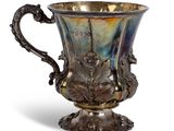 an antique silver cup with a dragon handle on a pedestal