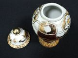 a white and gold vase with a lid on a black table