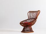 Une vieille chaise en osier, avec un coussin rouge, est posée sur une surface blanche.