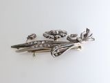 three silver brooches with flowers on them on a white surface