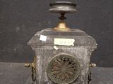 a small metal clock on a stand with a sticker on it