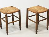 two wooden stools with wicker seats on a white surface