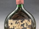 an old green glass bottle with a pink cap on a gray surface