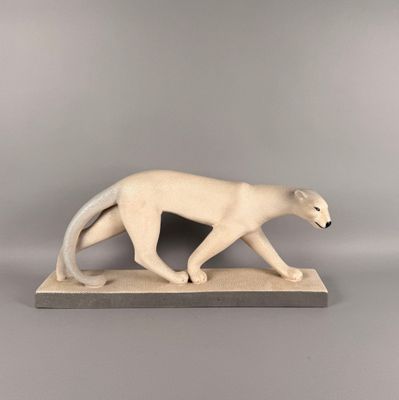 une sculpture blanche représentant un chat marchant sur un socle en bois