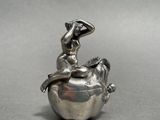 silver figurine of a woman sitting on top of an apple