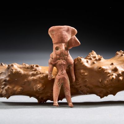 figurine représentant un homme coiffé d'un chapeau, assis sur un morceau de bois