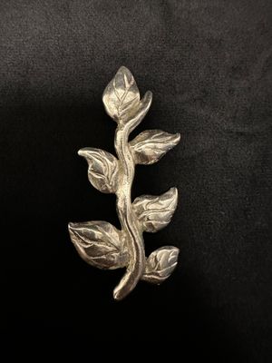 a close up of a silver brooch with leaves on a black background