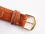 the brown leather watch strap has gold buckles on it