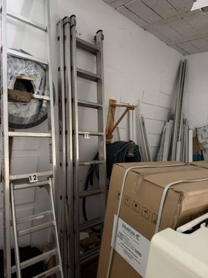 Des cartons et des échelles sont empilés dans une pièce aux murs blancs