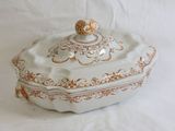 a white and gold covered dish on a white surface