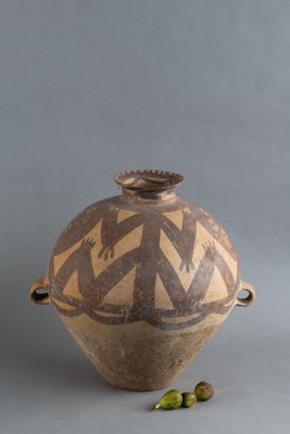 un vase marron orné d'un motif, à côté de quelques noix