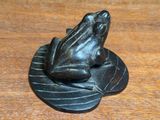 statue of a frog sitting on a leaf on a wooden table