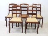 four wooden chairs with beige upholstered seats in front of a white wall