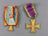 two medals and a cross on a table with a gray background