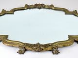 un miroir aux formes ouvragées posé sur une surface blanche, avec un fond blanc