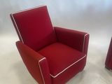 pair of red leather lounge chairs with white piping on the arms