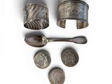three silver cuff bracelets, a spoon, and a spoon rest on a white surface