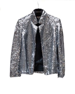 une veste à paillettes argentées suspendue à un cintre sur un mur blanc