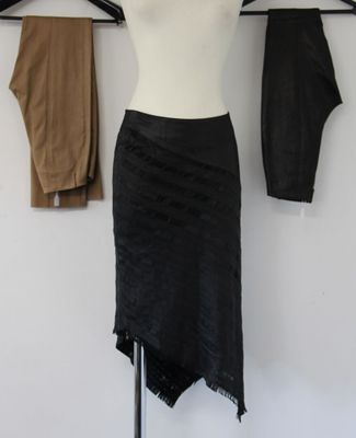 the black skirt is hanging on a clothes rack in front of a white wall