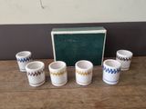 six cups and a box on a wooden table with a green box