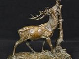 bronze sculpture of a stag standing next to a tree on a black background