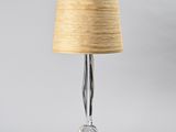 a glass table lamp with a beige shade on top of it