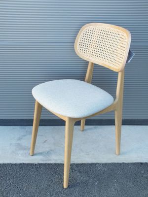 une chaise en bois avec une assise blanche, près d'un mur gris