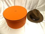 une boîte à chapeaux orange et un chapeau marron posés sur une surface blanche